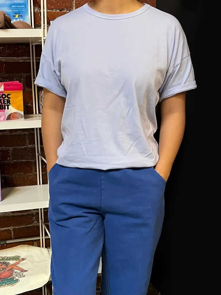 Person wearing a light blue Her Tee in 'Serenity' from Le Bon Shoppe and dark blue pants against a brick background | Twentyseven Toronto