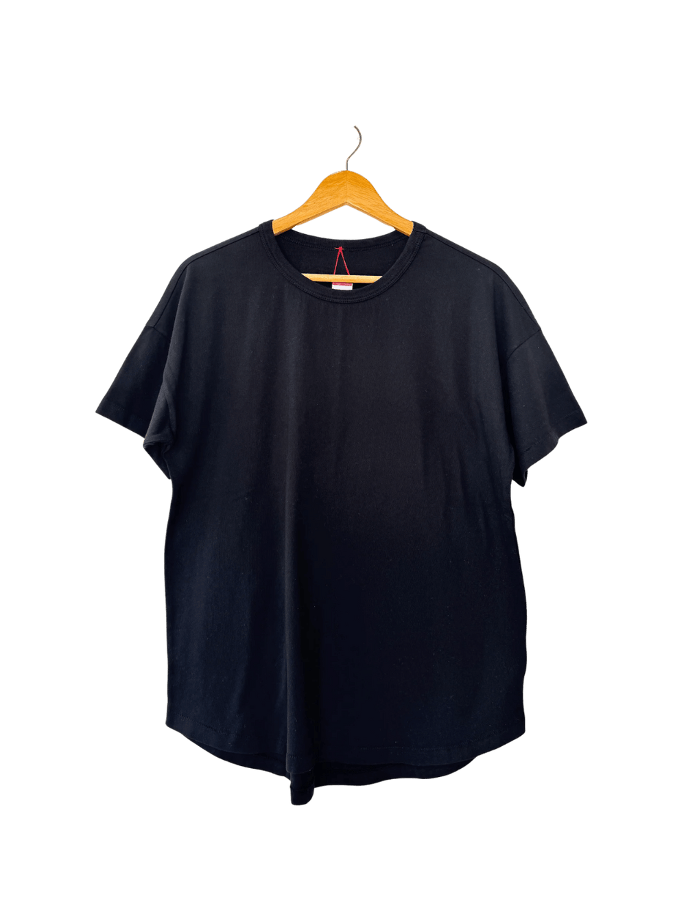 The Le Bon Shoppe Her Tee - True Black is displayed flat on a wooden hanger highlighting its curved hemline | Twentyseven Toronto