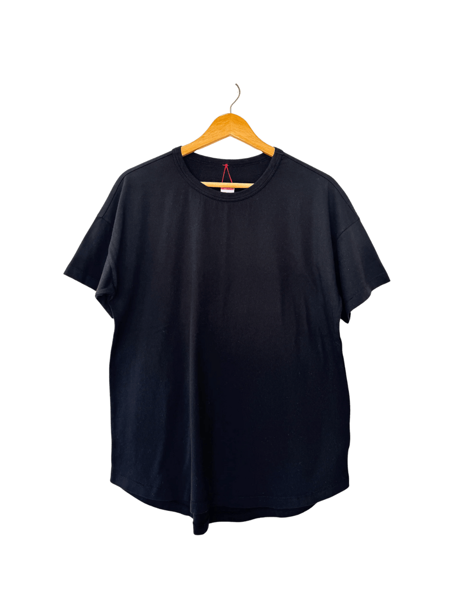 The Le Bon Shoppe Her Tee - True Black is displayed flat on a wooden hanger highlighting its curved hemline | Twentyseven Toronto