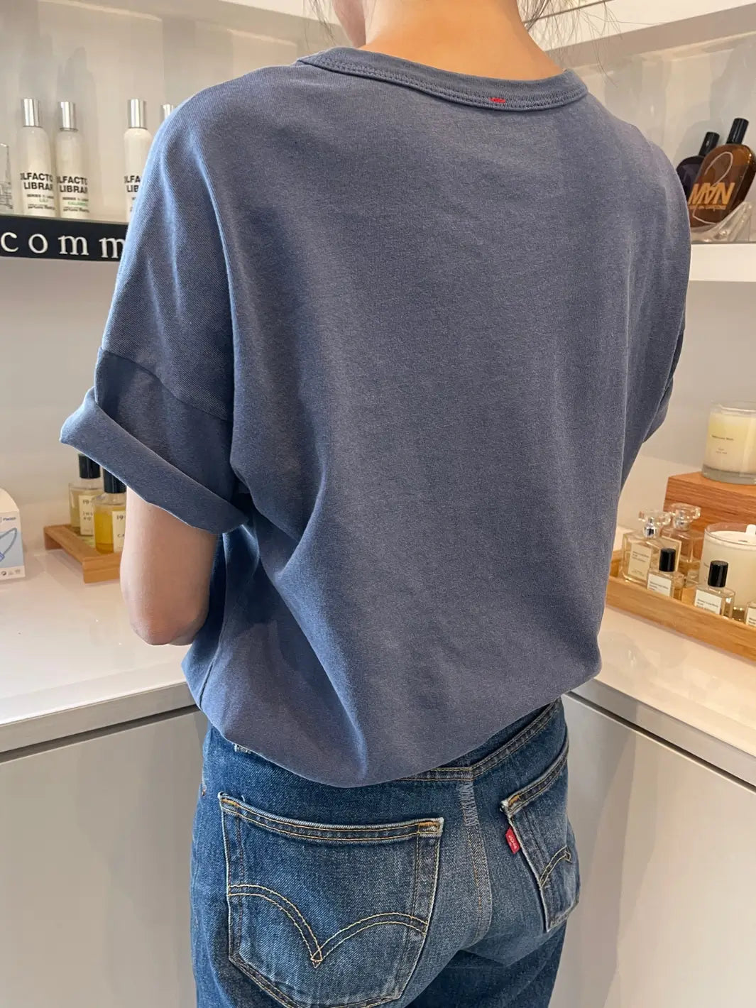 Back side of a person wearing a blue Her Tee in 'Vintage Navy' from Le Bon Shoppe and blue jeans standing indoors with products in the background | Twentyseven Toronto