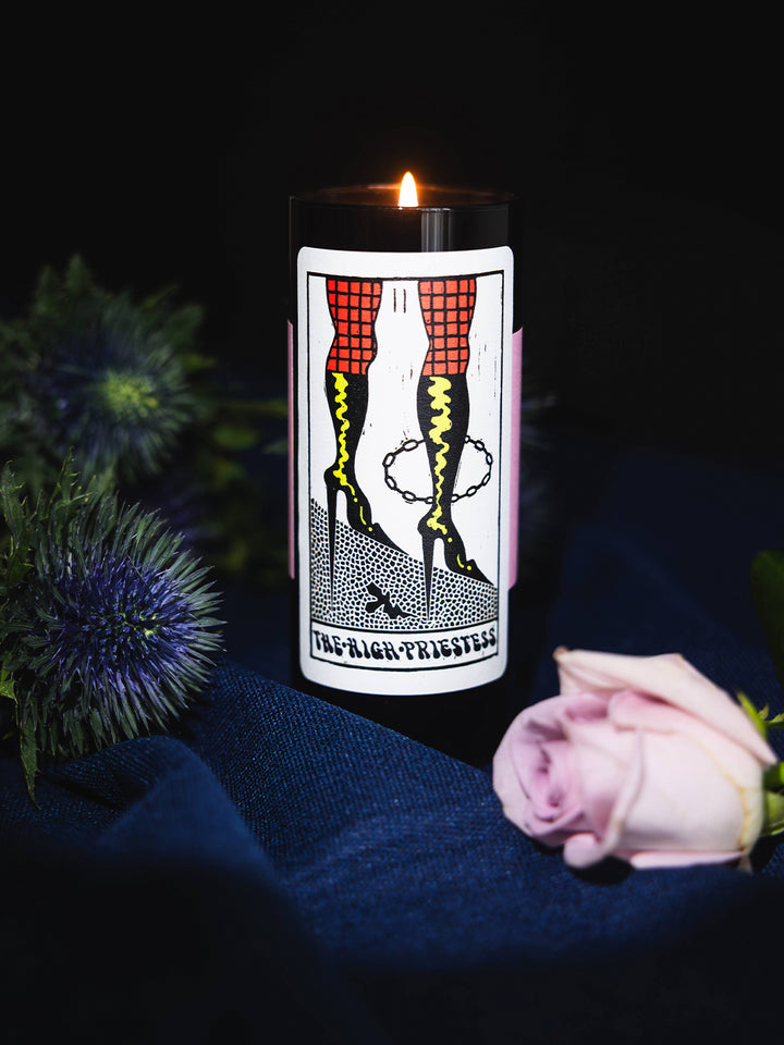 Lit High Priestess Tarot Candle styled with a pink rose and thistle against a dark backdrop | Twentyseven Toronto