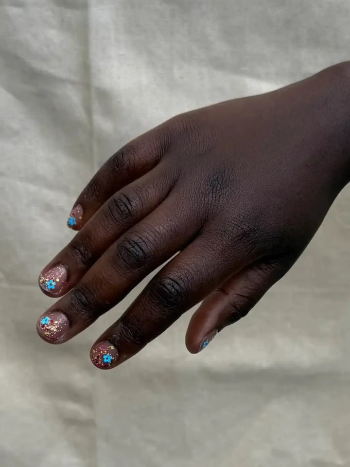 Close-up of a hand with glittery pastel pink, blue and yellow 'Hot Pants' nail polish by Death Valley Nails against a blurred natural background | Twentyseven Toronto