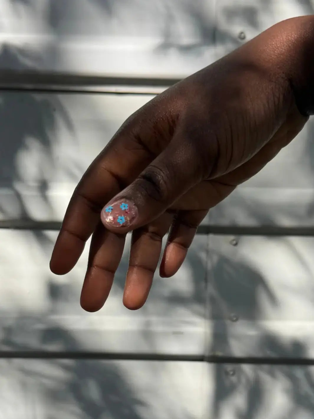Close-up of a hand with glittery pastel pink, blue and yellow 'Hot Pants' nail polish by Death Valley Nails against a blurred natural background | Twentyseven Toronto