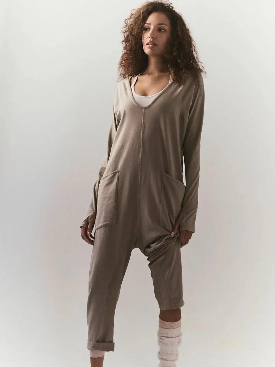 A front view shows a model with curly hair wearing the relaxed, slouchy Free People Hot Shot Long Sleeve Onesie - Sage Stone layered over a white tank top | Twentyseven Toronto