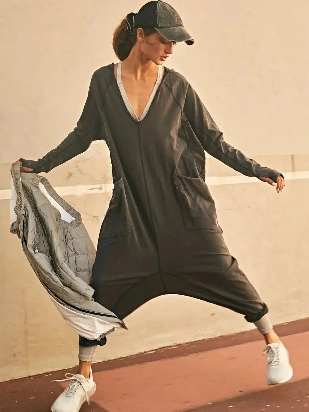 A model wearing the slouchy Free People Hot Shot Long Sleeve Onesie - Black paired with a baseball cap and white sneakers | Twentyseven Toronto