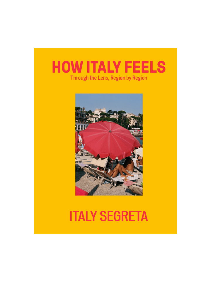 Front cover of How Italy Feels: Through the Lens, Region by Region by Italy Segreta, featuring a vibrant yellow background with red typography and a central photograph of a woman under a red beach umbrella | Twentyseven Toronto