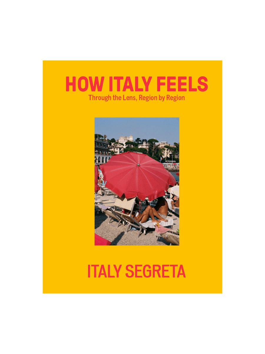 Front cover of How Italy Feels: Through the Lens, Region by Region by Italy Segreta, featuring a vibrant yellow background with red typography and a central photograph of a woman under a red beach umbrella | Twentyseven Toronto