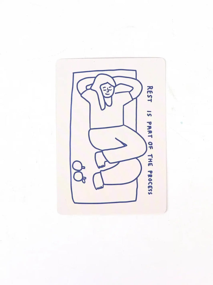 A single card from the How To Decide Deck from People I've Loved is centered on a white surface, displaying a minimalist blue line drawing of a person relaxing with the text "rest is part of the process" } Twentyseven Toronto