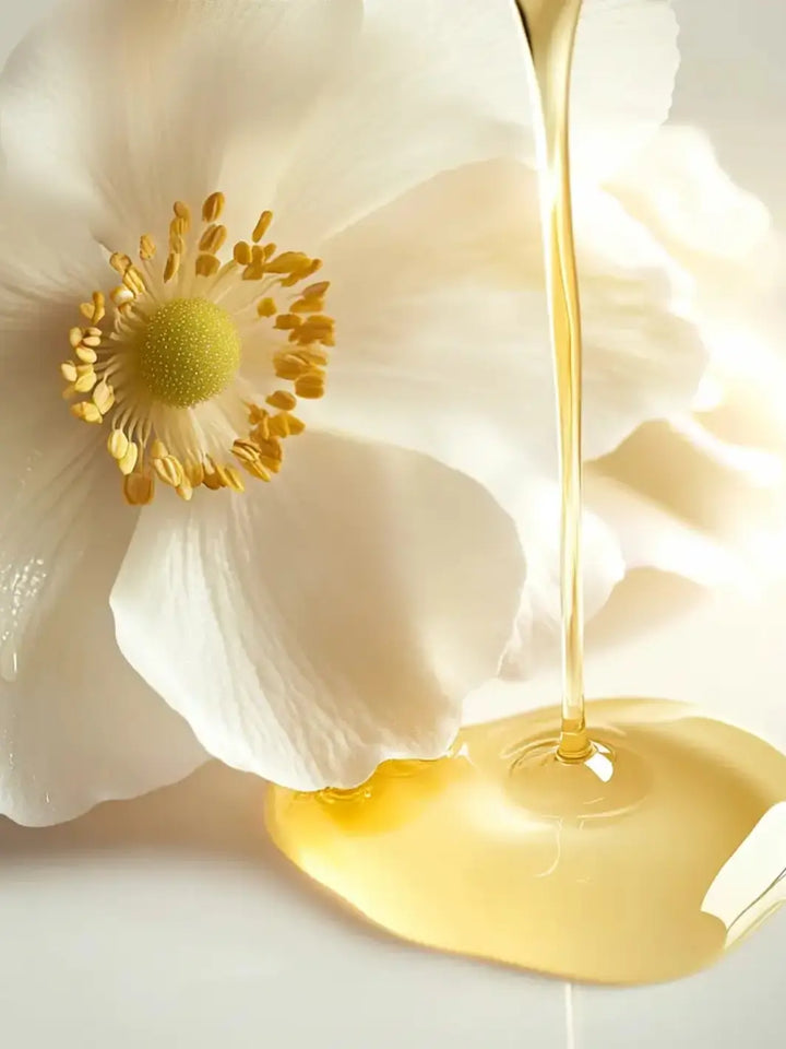 White flower with yellow center and a 'Huile Secret de Beauté' gold liquid from Leonor Greyl pouring onto it | Twentyseven Toronto