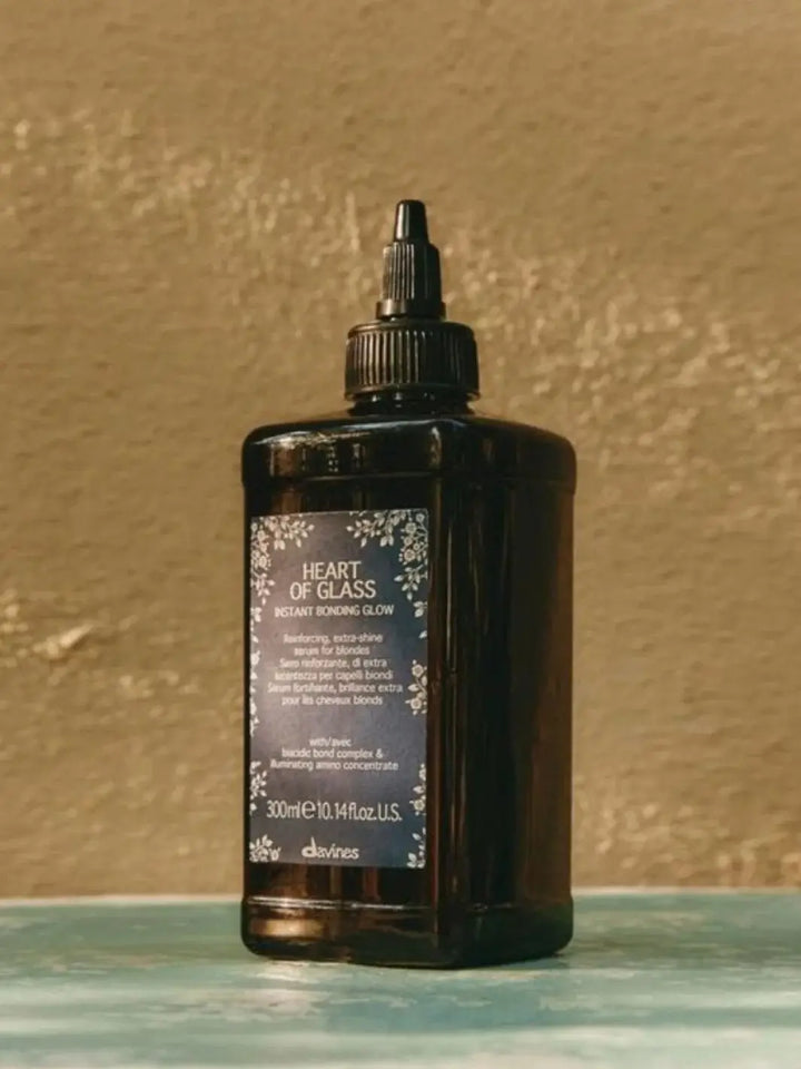 A dark bottle of Davines Heart of Glass Instant Bonding Glow sits on a textured surface | Twentyseven Toronto