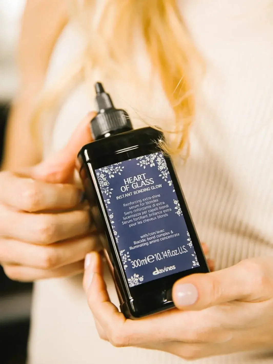 A person holds a dark bottle of Davines Heart of Glass Instant Bonding Glow hair serum with both hands | Twentyseven Toronto