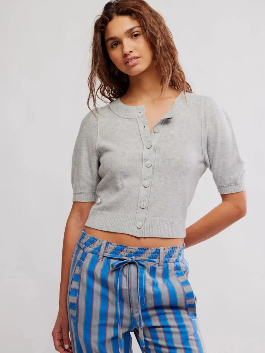 A model poses from the front wearing the cropped, short-sleeve Free People Isla Solid Cardi - Mineral Grey styled with blue striped trousers | Twentyseven Toronto