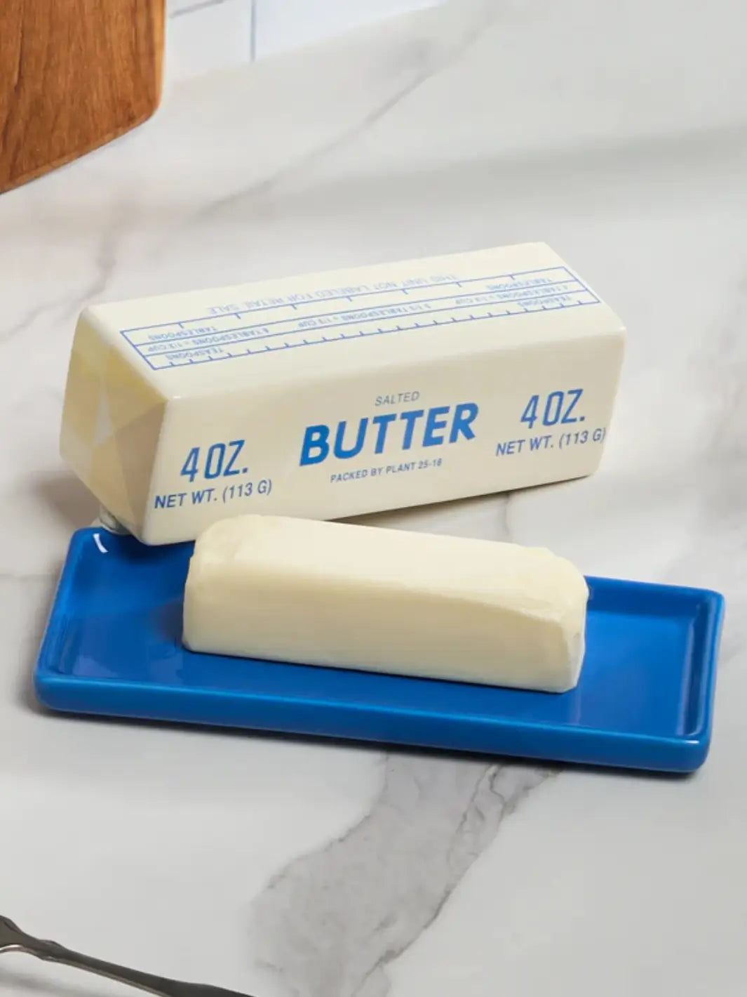 A close-up lifestyle view highlights the lid of the Item - Butter Stick Butter Dish from Fishs Eddy resting behind a real stick of butter on its vibrant blue ceramic tray | Twentyseven Toronto
