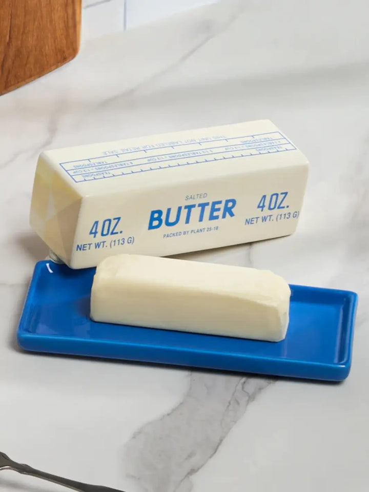 A close-up lifestyle view highlights the lid of the Item - Butter Stick Butter Dish from Fishs Eddy resting behind a real stick of butter on its vibrant blue ceramic tray | Twentyseven Toronto