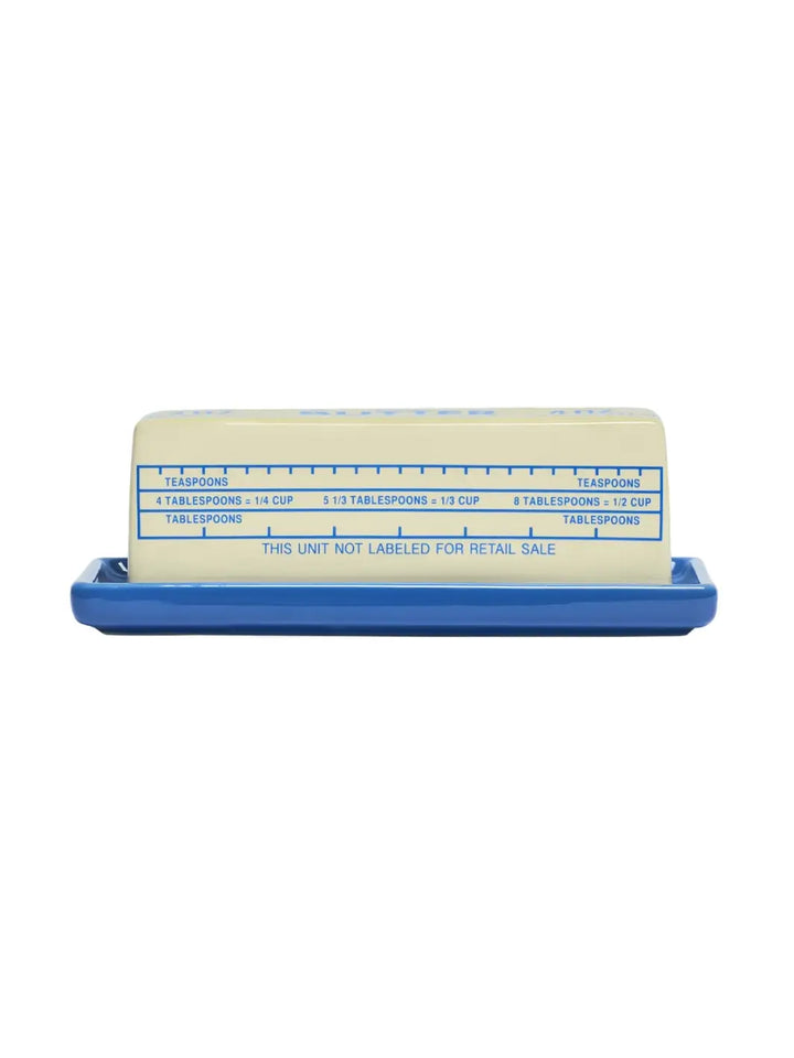 A side view of the ceramic Item - Butter Stick Butter Dish from Fishs Eddy, featuring blue measurement markings for tablespoons and teaspoons on its cream-coloured lid | Twentyseven Toronto