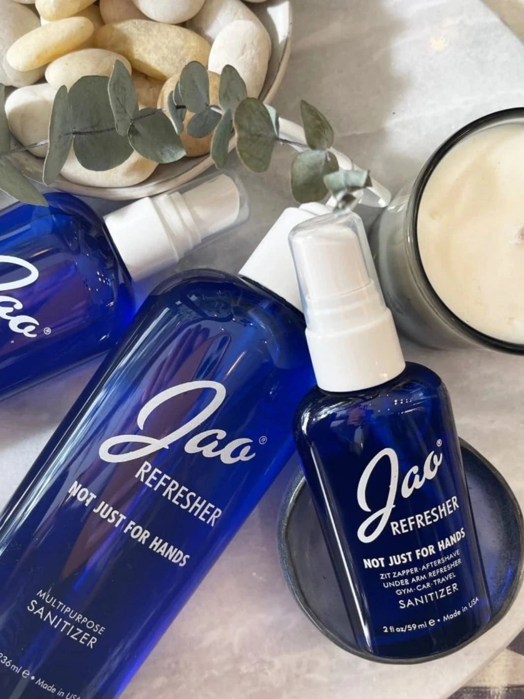 Different sizes of blue bottles of Jao Refresher on a surface with pebbles and a candle in the background 2 fl oz | Twentyseven Toronto