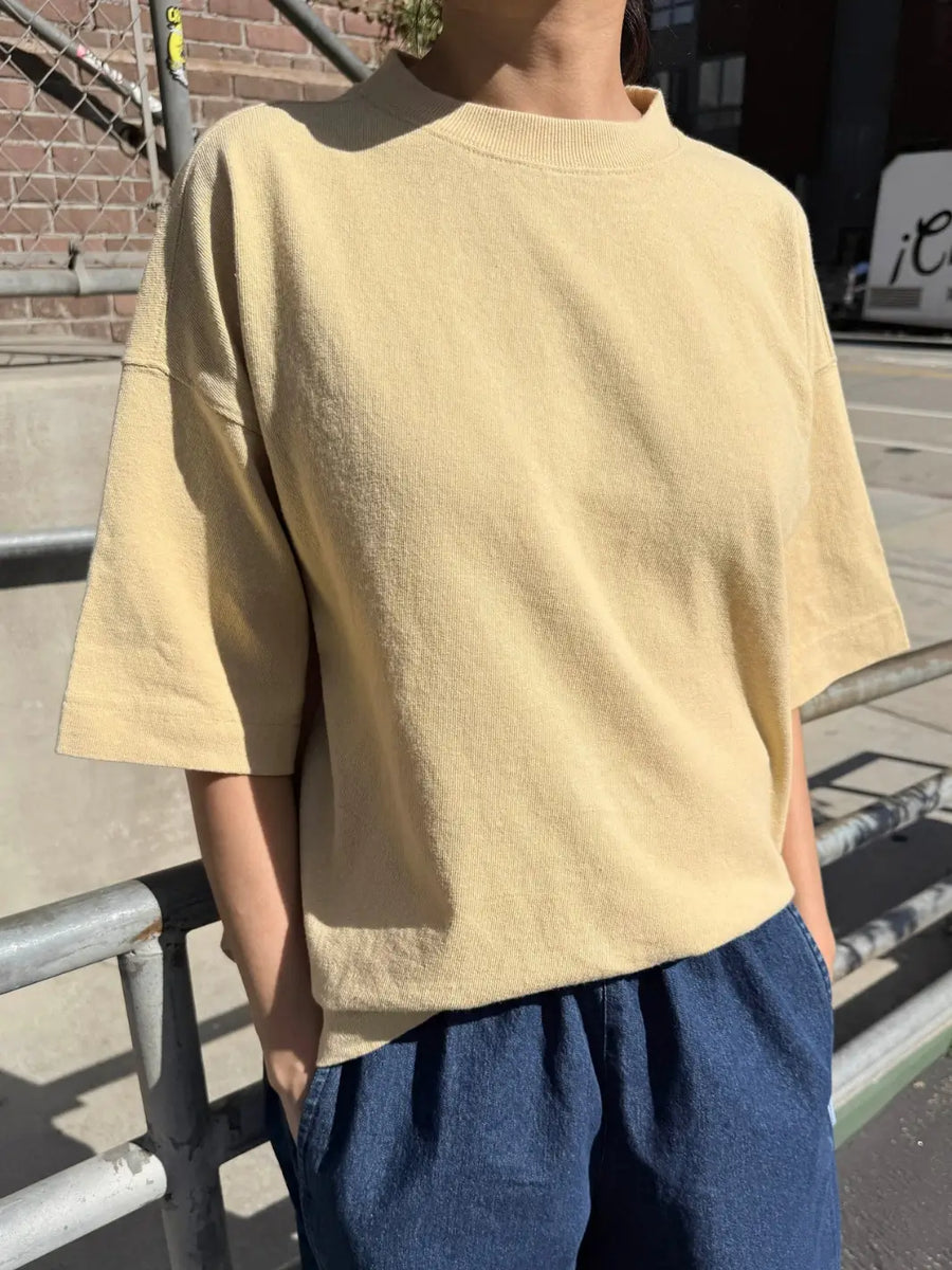 A person models the yellow oversized, short-sleeved Le Bon Shoppe Jayden Tee - Butter while standing outdoors next to a metal railing | Twentyseven Toronto