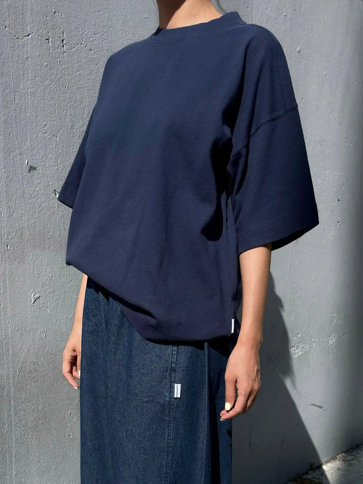 A person wears an oversized, dark navy Le Bon Shoppe Jayden Tee in Midnight paired with a denim skirt while standing against a textured gray concrete wall | Twentyseven Toronto