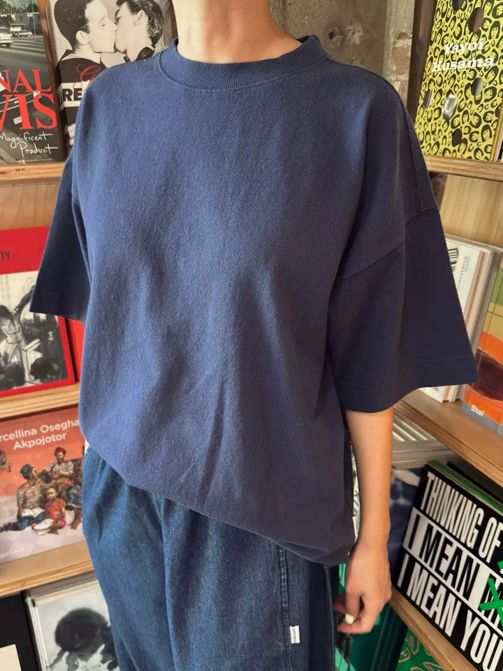 A person models an oversized Le Bon Shoppe Jayden Tee in Midnight while standing indoors in front of wooden bookshelves filled with books | Twentyseven Toronto