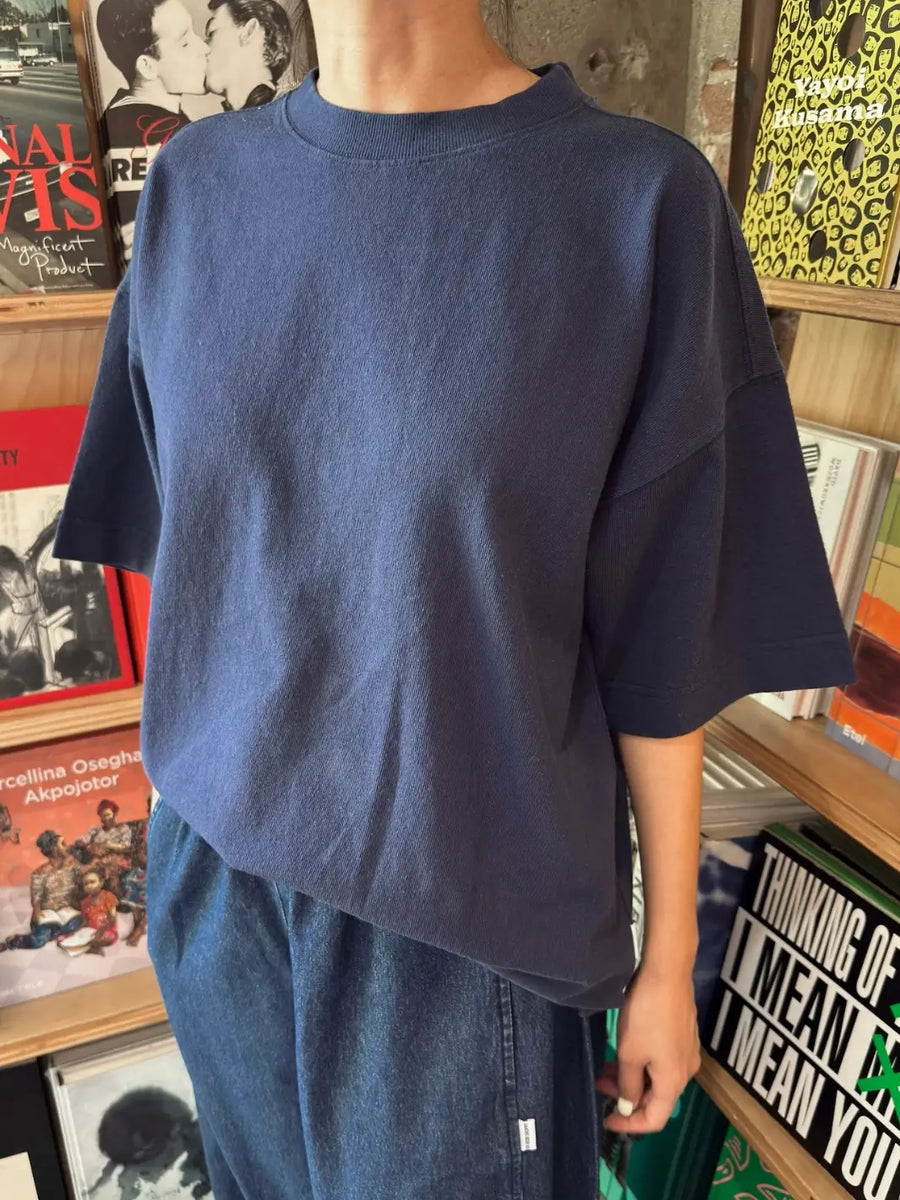 A person models an oversized Le Bon Shoppe Jayden Tee in Midnight while standing indoors in front of wooden bookshelves filled with books | Twentyseven Toronto