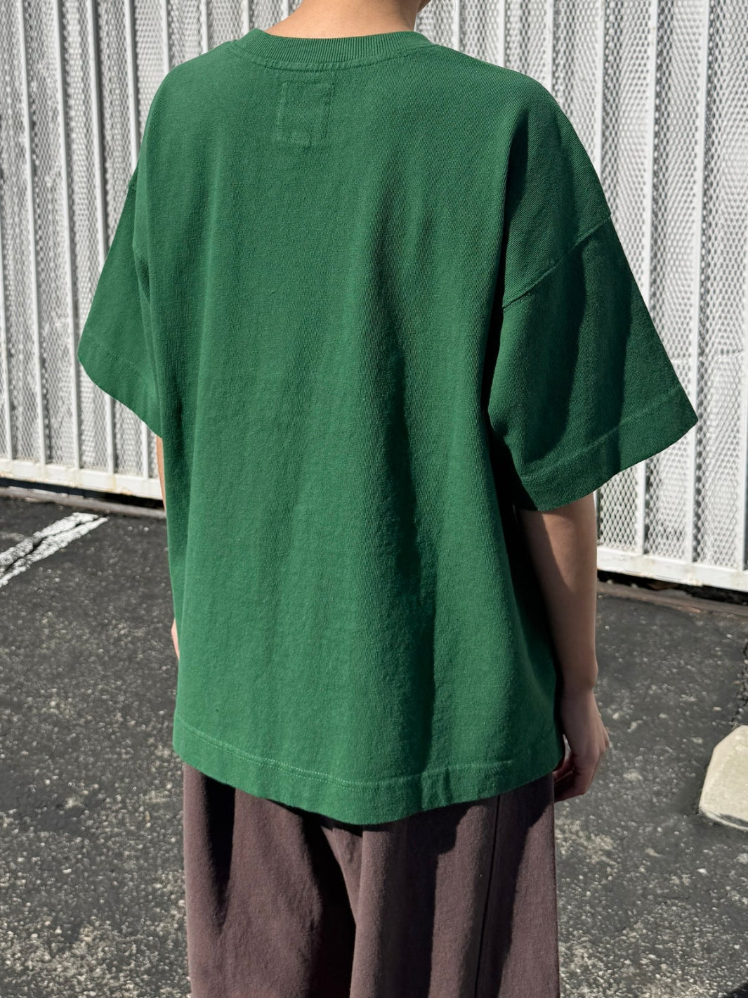 Person wearing dark green 'Jayden Tee' t-shirt in 'Moss Green' from Le Bon Shoppe with brown pants in an outdoor setting, back view | Twentyseven Toronto