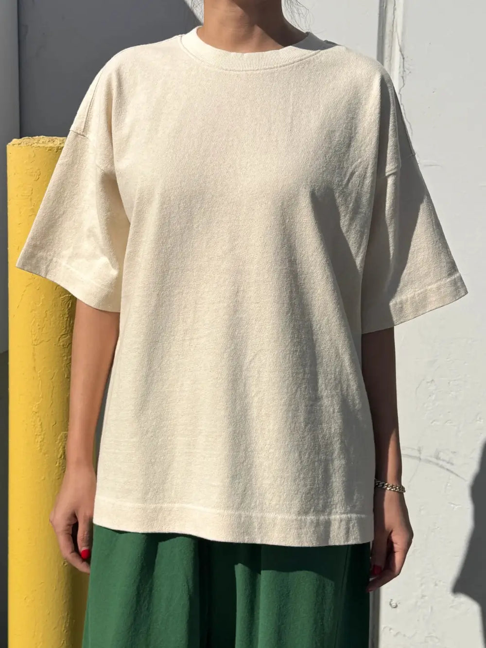 Person wearing cream 'Jayden Tee' t-shirt in 'Naturel' from Le Bon Shoppe on a white background with yellow object | Twentyseven Toronto