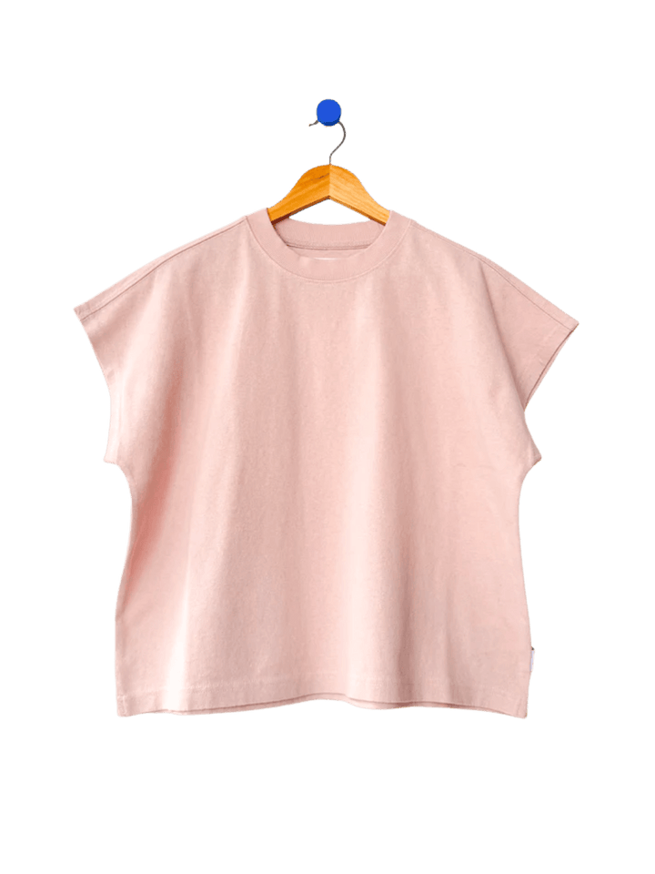 A boxy, crewneck Le Bon Shoppe Jeanne Tee in Baby Pink featuring extended cap sleeves hangs from a wooden hanger | Twentyseven Toronto