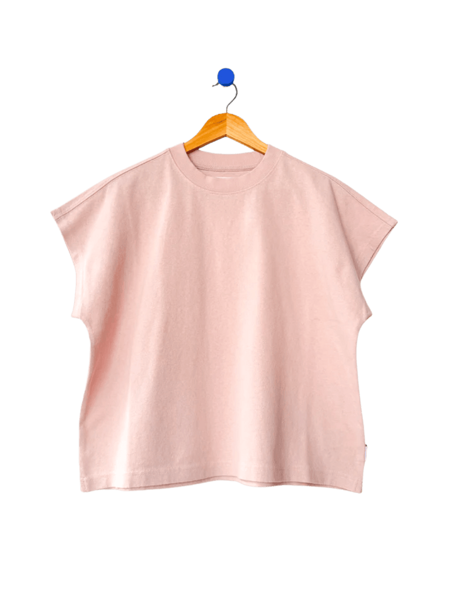 A boxy, crewneck Le Bon Shoppe Jeanne Tee in Baby Pink featuring extended cap sleeves hangs from a wooden hanger | Twentyseven Toronto
