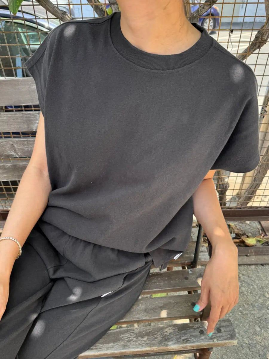 A person sits on a wooden bench wearing a dark, washed charcoal Le Bon Shoppe Jeanne Tee in Dark Slate with matching sweatpants | Twentyseven Toronto