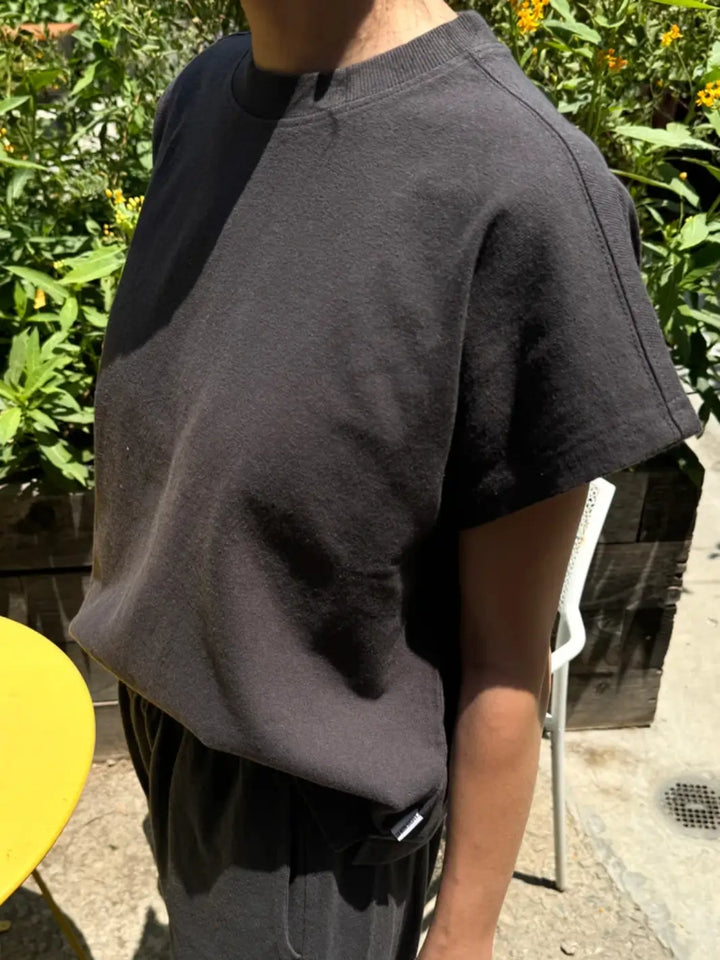 A close-up side view shows a person wearing a boxy, short-sleeved Le Bon Shoppe Jeanne Tee in Dark Slate outdoors  | Twentyseven Toronto