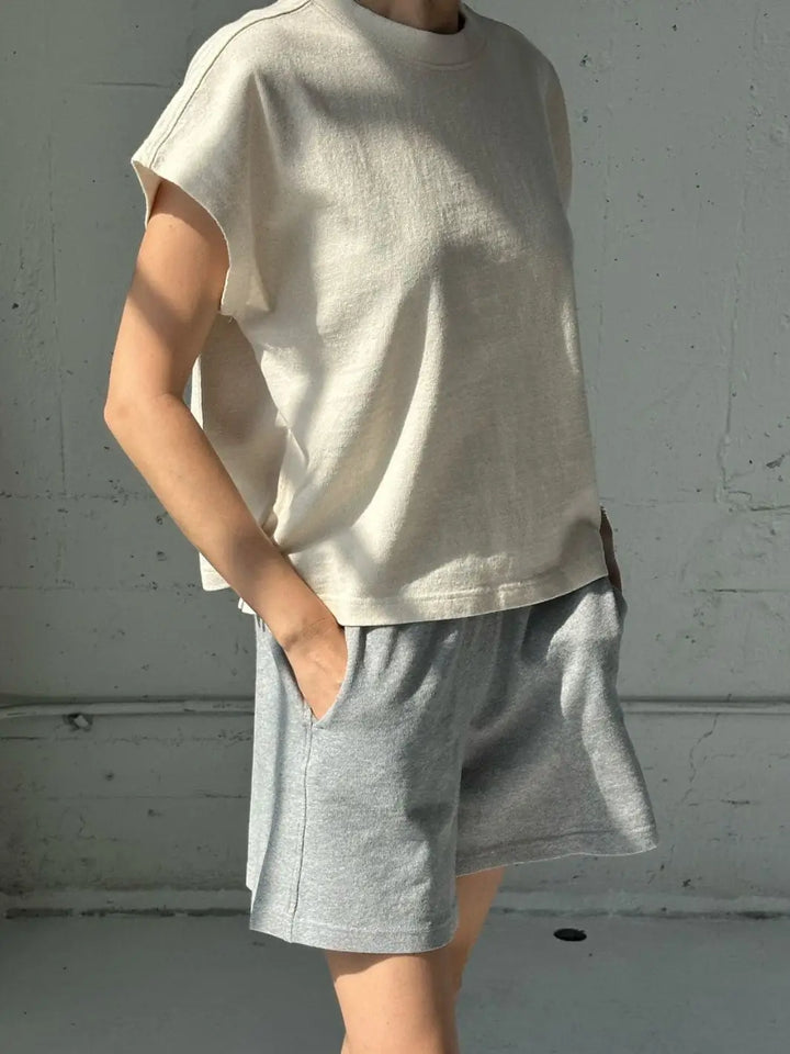 A person stands in a sunlit room wearing a boxy Le Bon Shoppe Jeanne Tee in Naturel and casual heather gray sweat shorts | Twentyseven Toronto