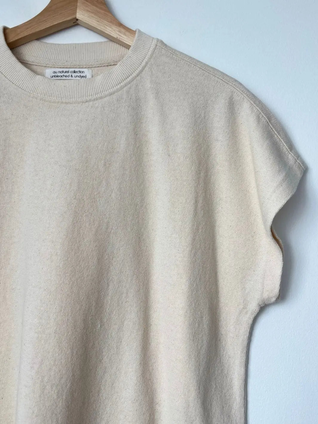 A close up of an off-white Le Bon Shoppe Jeanne Tee in Naturel with an oversized fit hanging from a wooden hanger | Twentyseven Toronto