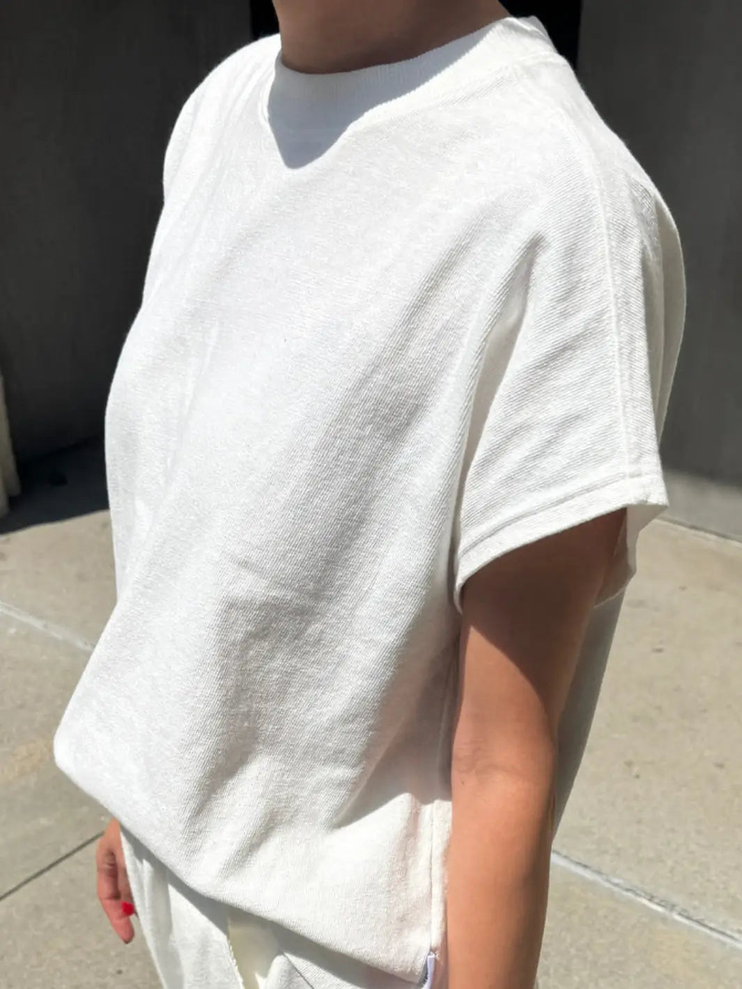 A side angle shot highlights the loose cap sleeves and textured knit fabrication of the Le Bon Shoppe Jeanne Tee in White Cotton worn by a model | twentyseven Toronto