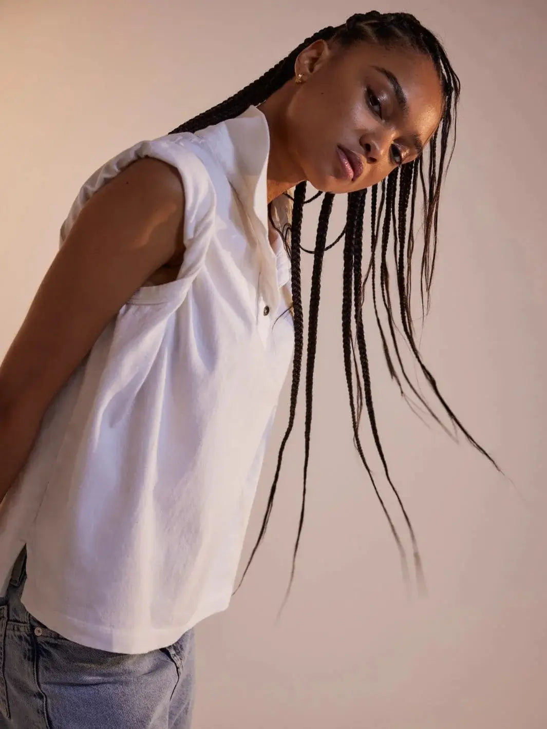 A model with long braids poses dynamically from a side angle to showcase the flowy fit of the Free People Keep On Polo - Clean Ivory | Twentyseven Toronto
