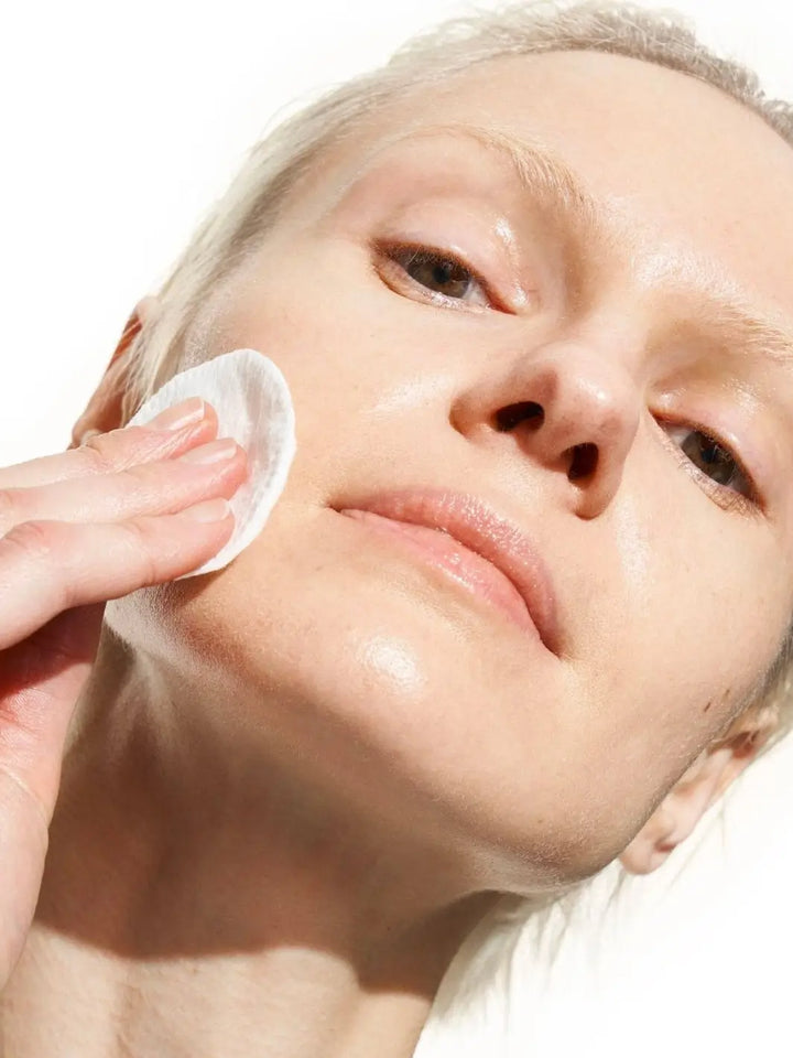 Woman cleaning their face with Doré La Micellaire Botanical Cleansing Water using a cotton pad against a white background | Twentyseven Toronto