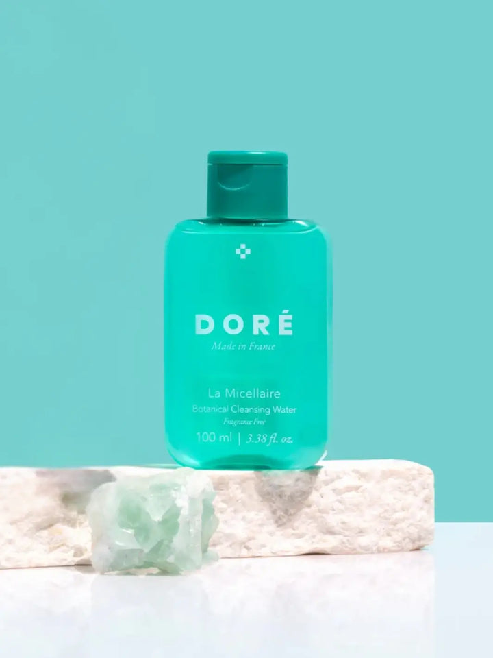 Green 100ml bottle of Doré La Micellaire Botanical Cleansing Water on a white marble slab and light blue background | Twentyseven Toronto