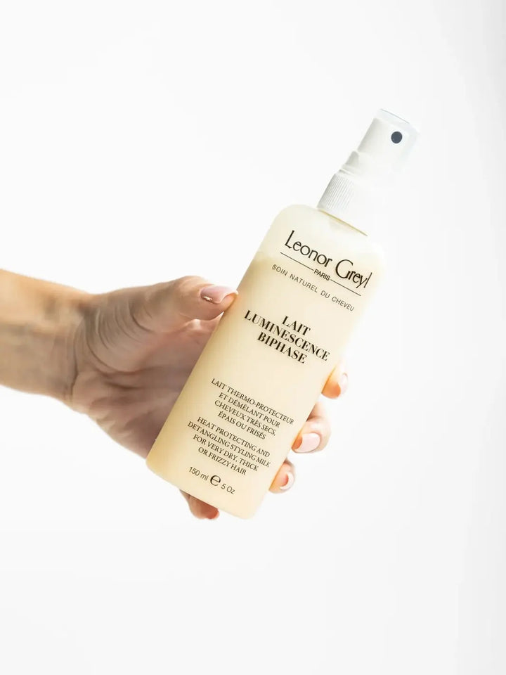 Hand holding a 150ml bottle of Leonor Greyl 'Lait Luminescence Biphase' against a white background | Twentyseven Toronto