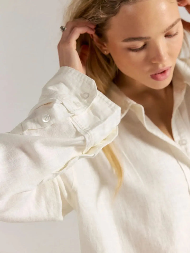 Woman wearing a white button down shirt by Free People We the Free 'Laurel Linen Button Down Top' in 'Clean Ivory' against white background, close up view | Twentyseven Toronto