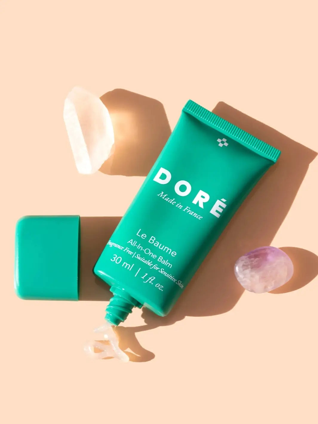 Green 30ml tube of Doré Skincare 'Le Baume' with cap off and product oozing out on a beige background | Twentyseven Toronto