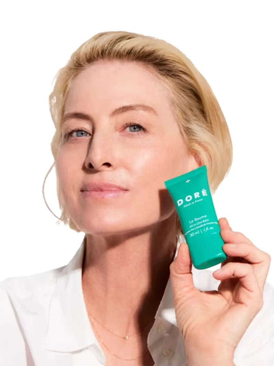 Woman holding a green tube of Doré Skincare 'Le Baume' against a white background | Twentyseven Toronto