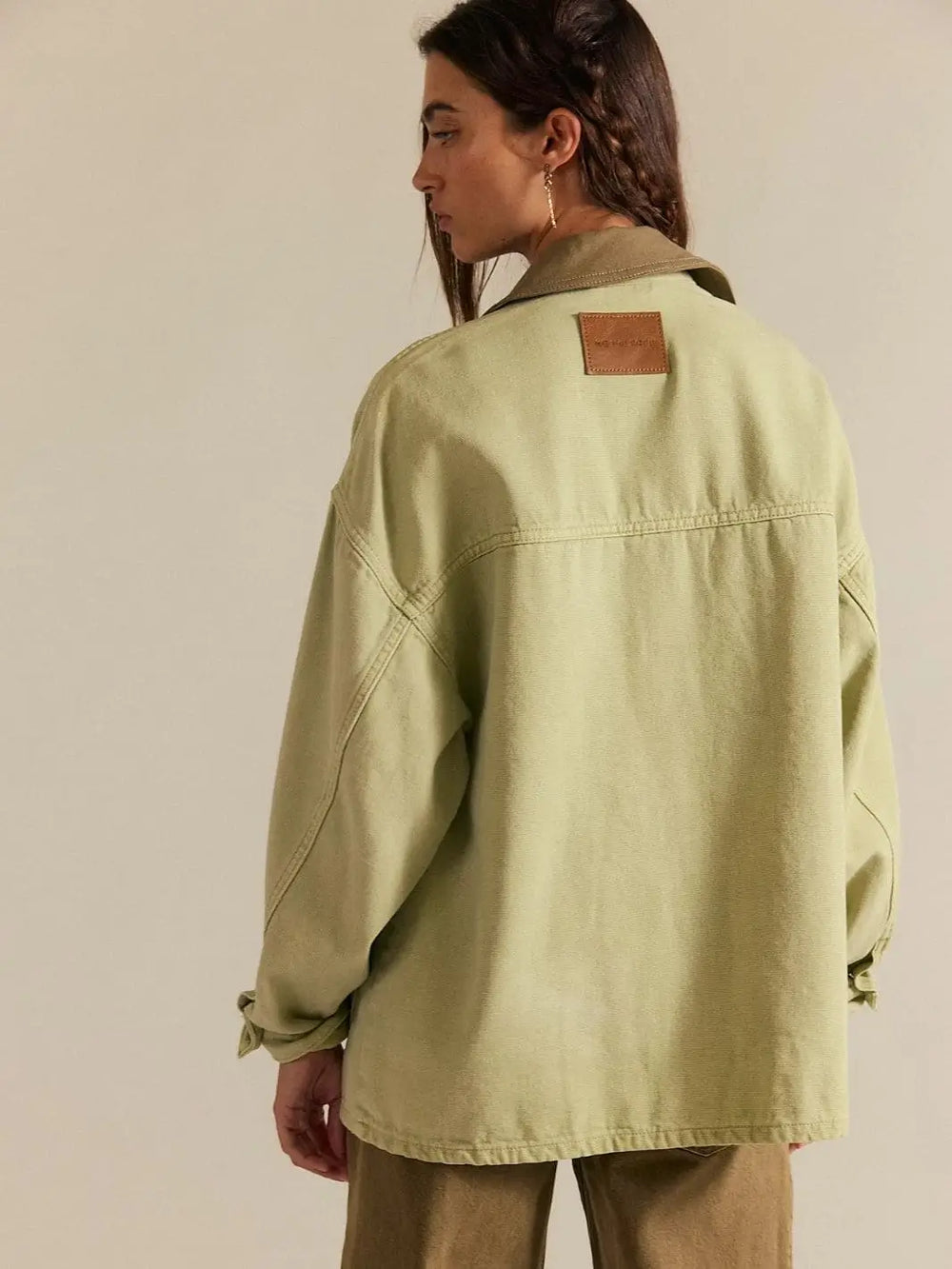 A three-quarter back view emphasizes the leather brand patch and horizontal seam detailing on the Free People Lemon Denim Jacket in Washed Sage | Twentyseven Toronto