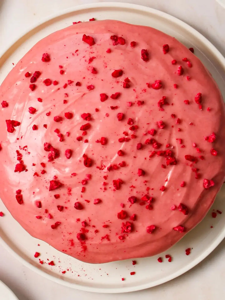 A top-down view shows a round cake made from the Glazed Cake Co Lemon Raspberry Cake Kit covered in smooth pink icing and topped with crushed dried raspberries | Twentyseven Toronto