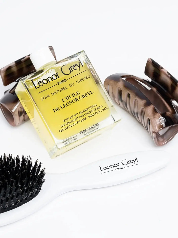 Leonor Greyl hair care products including a glass bottle of 'L’Huile de Leonor Greyl', brush, and clips on a white background | Twentyseven Toronto