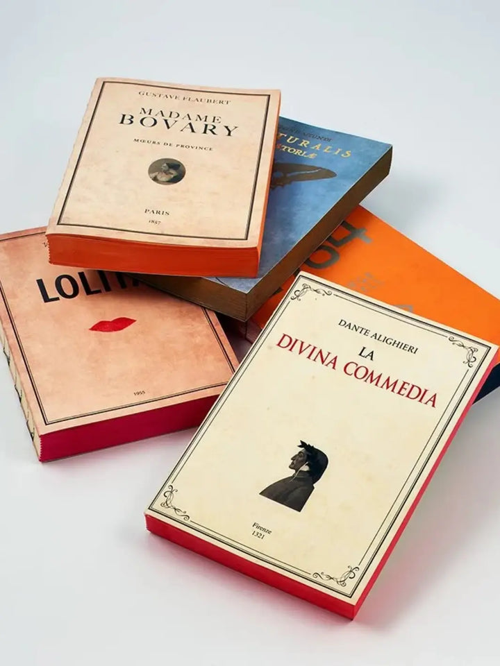 Five notebooks from the Slow Design Libri Muti collection, including titles like Madame Bovary and La Divina Commedia, are scattered to showcase their literary-inspired covers and brightly coloured hand-painted edges | Twentyseven Toronto