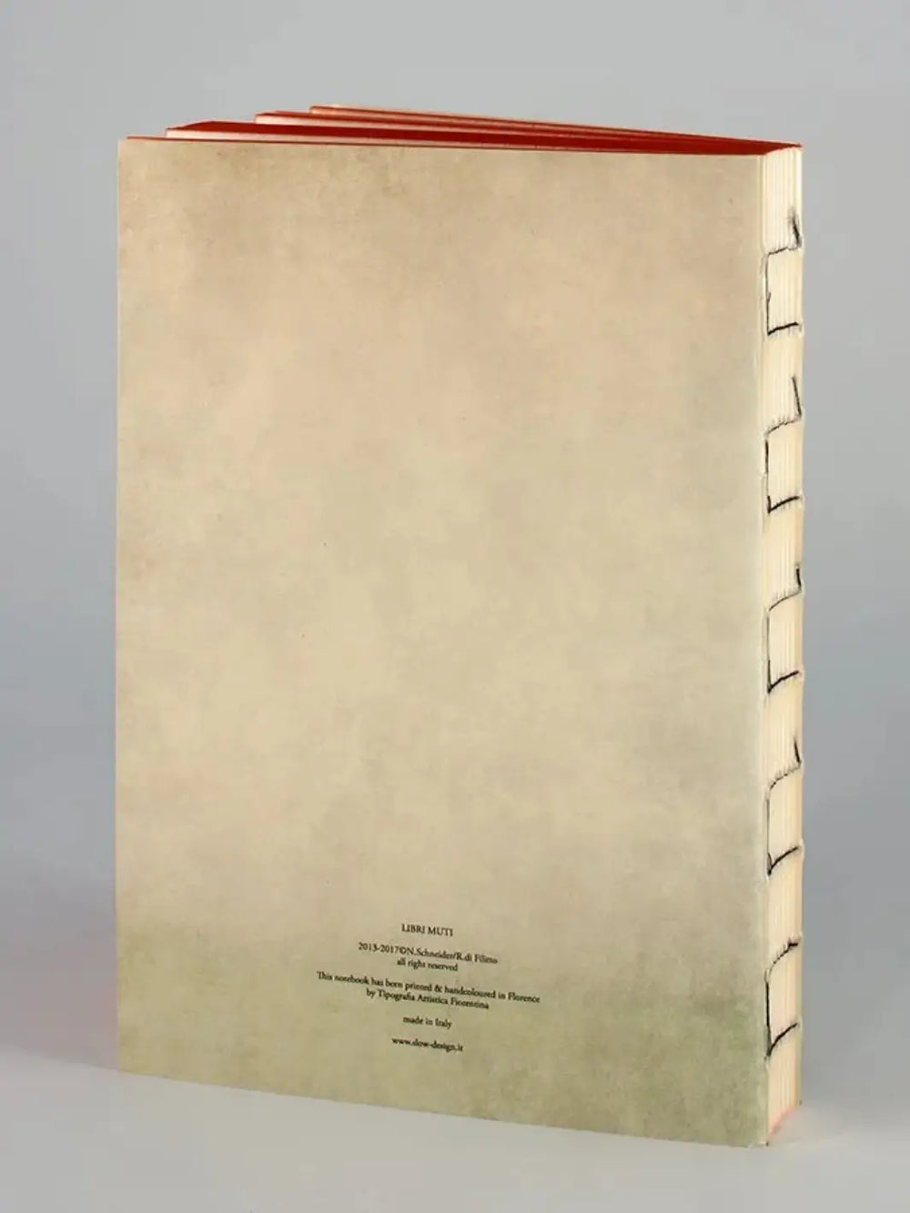 The back cover of a Jungle Book notebook from the Slow Design Libri Muti collection shows a clean, cream-colored surface with small publishing details at the bottom, an exposed hand-stitched spine, and orange hand-painted edges along the top | Twentyseven Toronto