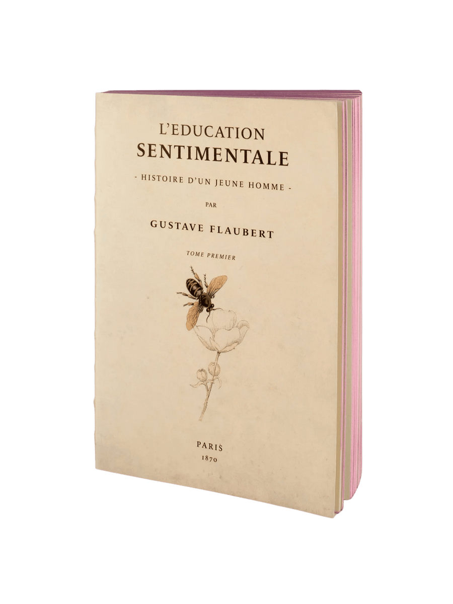 The front cover of a cream notebook from the L’Education Sentimentale from the Slow Design Libri Muti collection features the title by Gustave Flaubert above an illustration of a bee on a flower, framed by bright pink page edges | Twentyseven Toronto