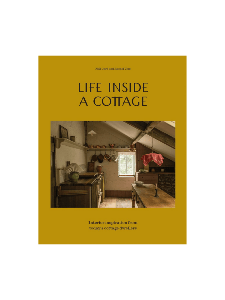 Book cover for Life Inside A Cottage by Nell Card and Rachel Vere features a mustard-yellow background with a central photo of a cozy, low-ceilinged cottage kitchen filled with copper pots and rustic charm | Twentyseven Toronto
