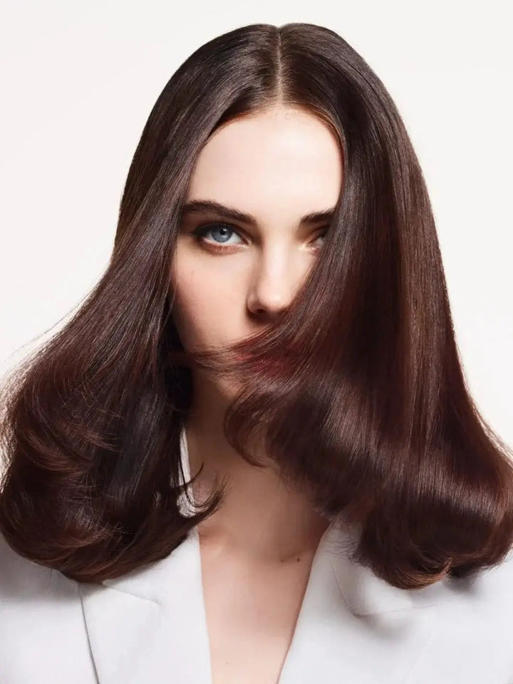A close-up portrait of a woman with bouncy, voluminous brunette hair blowing across her face highlights the lightweight hydration of Hair by Sam McKnight Light Nourish Conditioner | Twentyseven Toronto