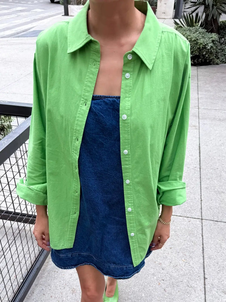 Person wearing 'Light Weight Owen Shirt' in 'Green Bud' from Le Bon Shoppe over a blue denim dress on a city street | Twentyseven Toronto