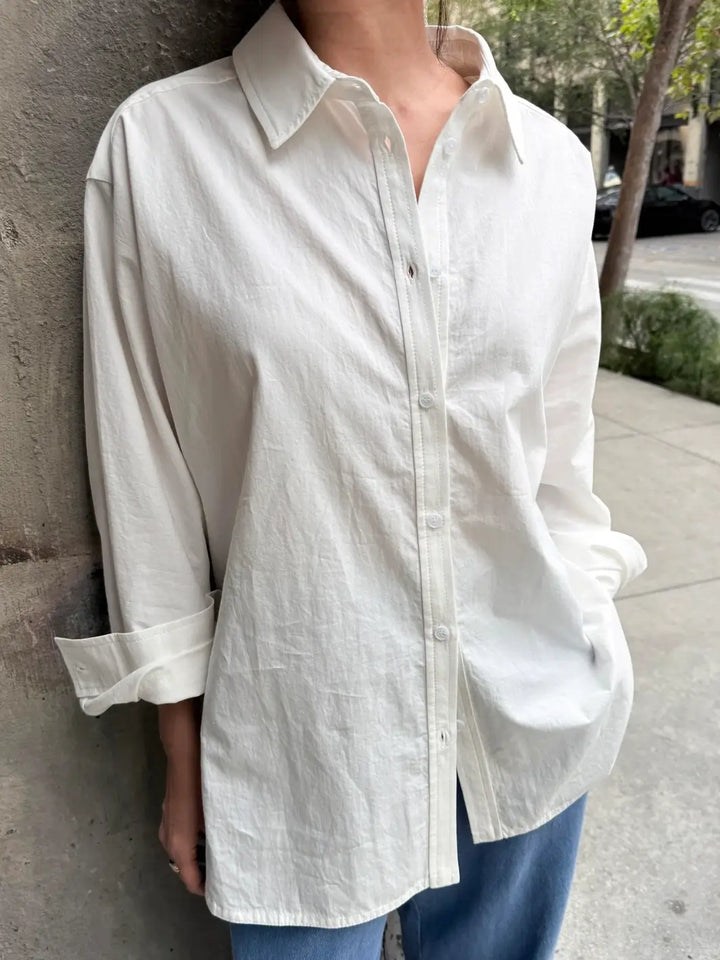 Person wearing a button up 'Light Weight Owen Shirt' in 'White' from Le Bon Shoppe and blue pants against a concrete wall | Twentyseven Toronto